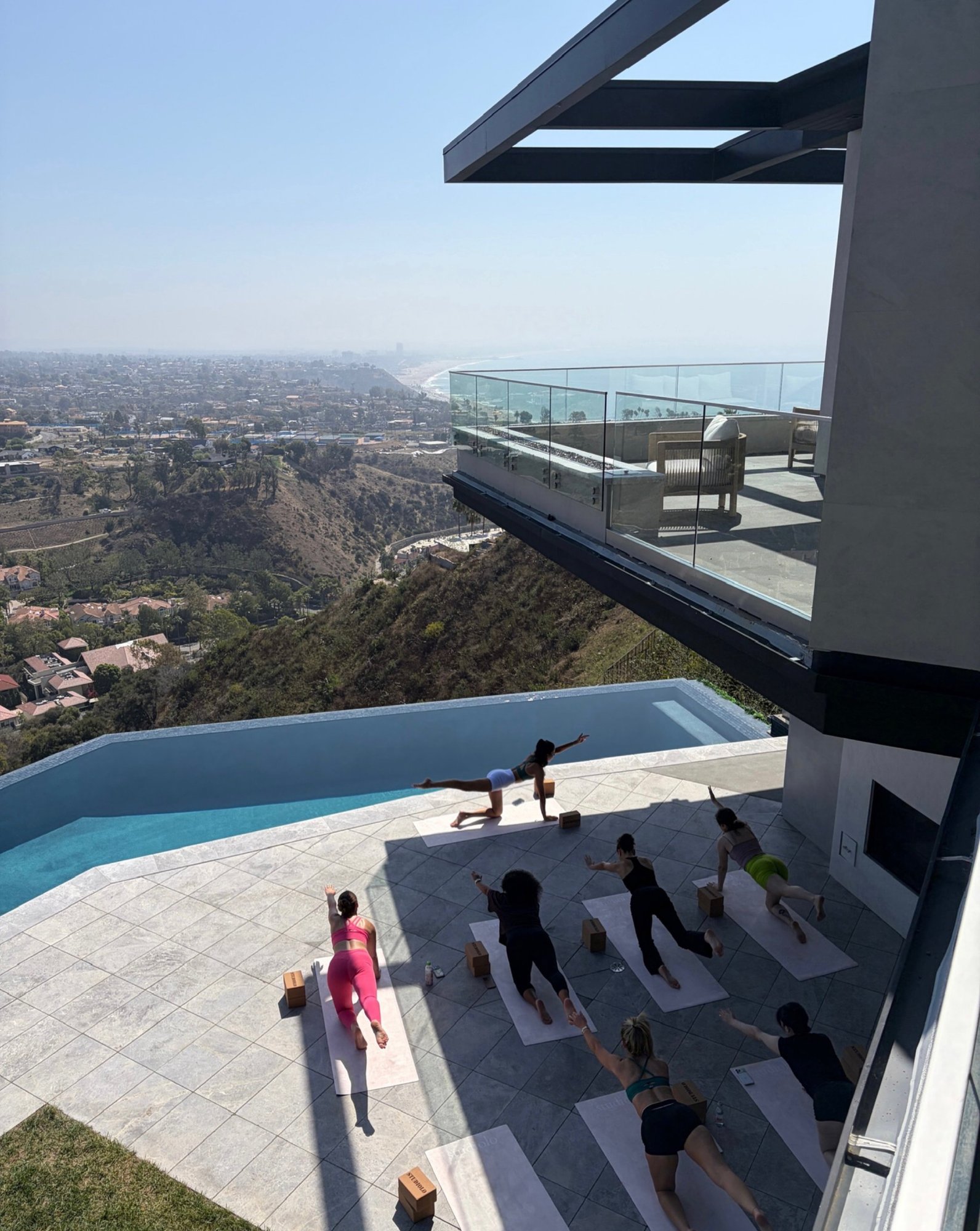 a group class on a terrace beside an infinity pool, high above the coast